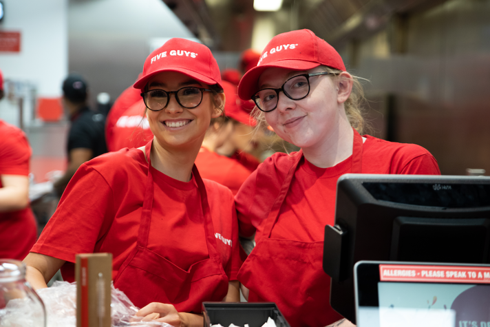 An image of two Five Guys employees smiling behind a till.