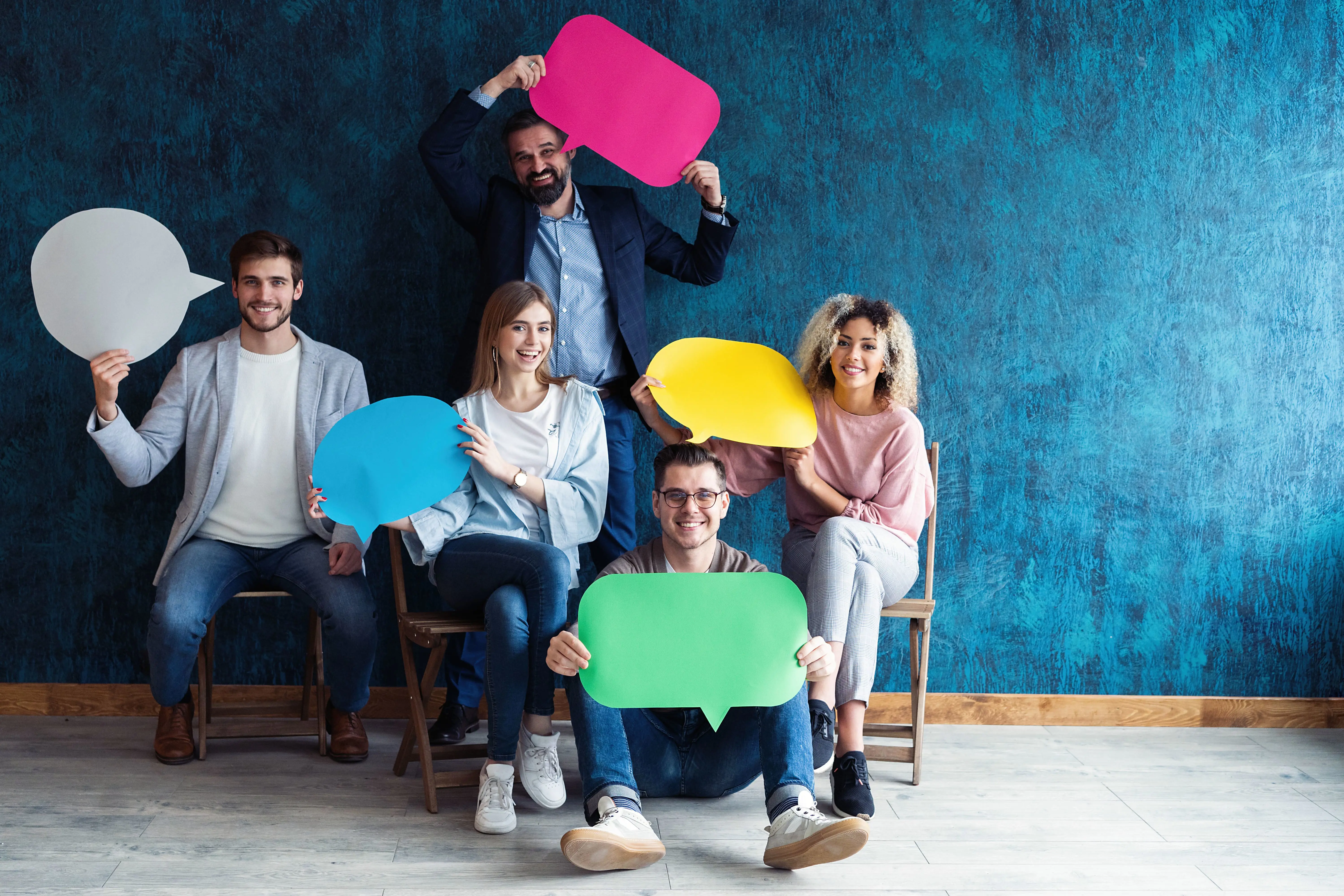 Five people sitting down smiling and holding cardboard cutouts of speech bubbles.