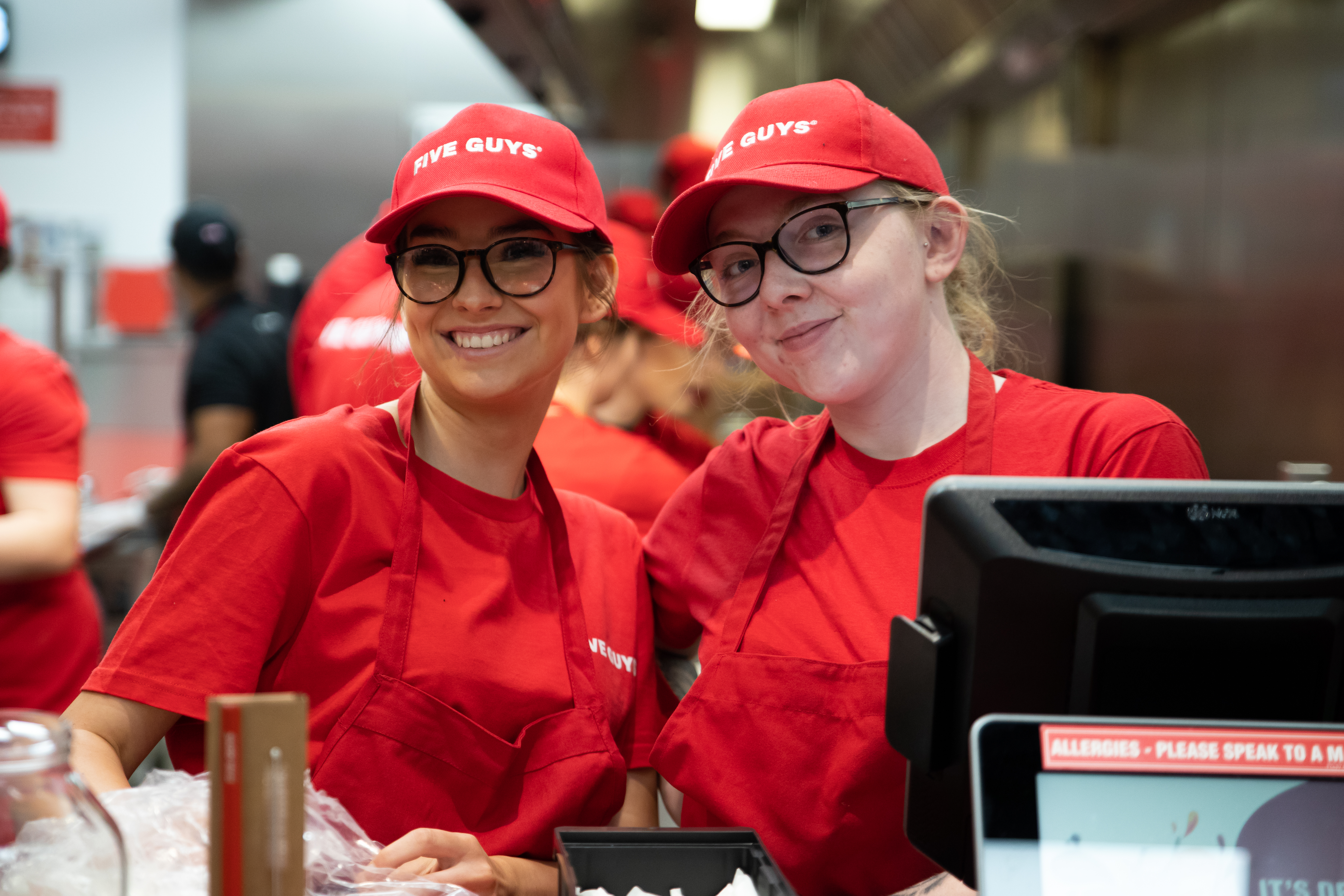 An image of two workers at Five Guys smiling next to a till